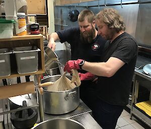 Pouring water over the grain that is in a fine woven cloth within a big stainless steel pot.