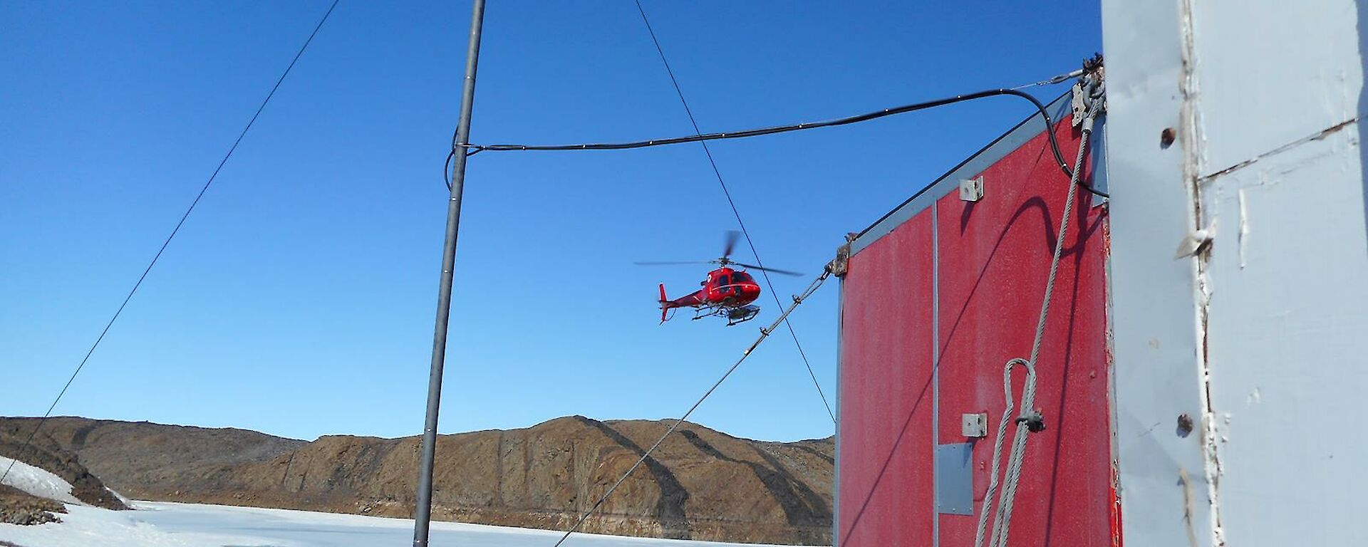 A red squirrel helicopter flying over the frozen fjord as it comes into land at Watts Hut.