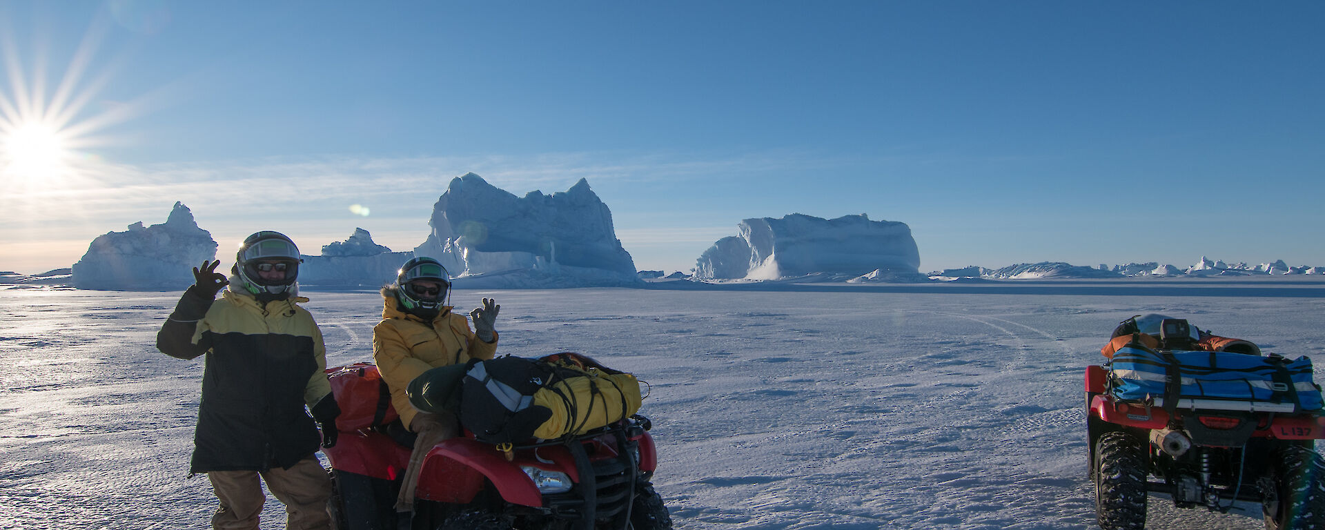 two expeditioners on the sea ice, one standing one sitting on a quad bike