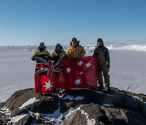 four expeditioners holding up the red ensign flag at Wilkins Cairn