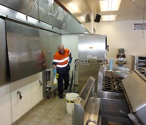 The chef with cleaning towels in hand cleaning behind the stoves and ovens.