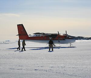 The Twin Otter aircraft on the sea ice in front of station with rocky islands in the background.