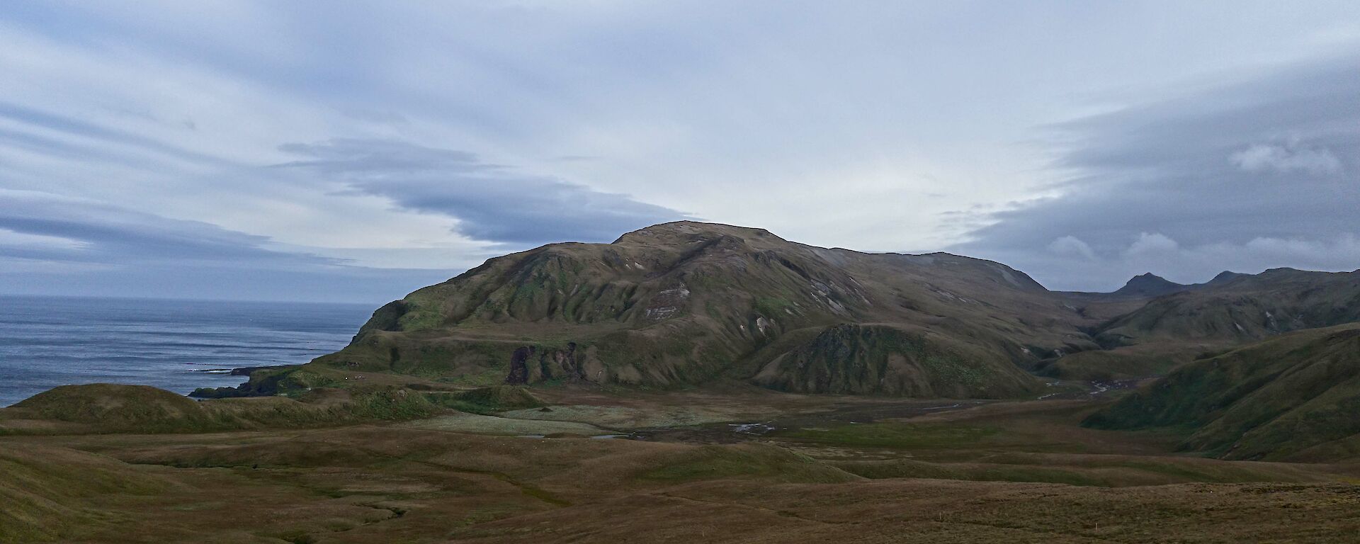 Green Gorge basin covered in greenery, shrouded by a gloomy sky with water in the background