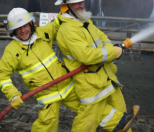 Two male expeditioners smile while holding a fire hose that is spraying water
