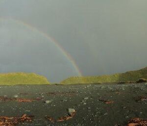 Panoramic landscape shot of macquarie island featuring green hills, ocean on left and a full rainbow — breathtaking