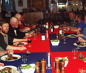 A long, wide table with expeditioners seated either side, and wine, food and candles