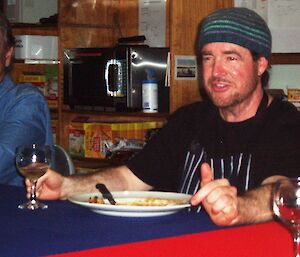 Chef Benny is shown relaxing in uniform at a dinner table, wine in hand