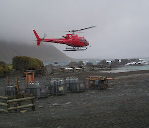 A helicopter lands amongst cargo on a dark and pebble covered beach