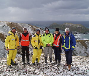 Mixed group of expeditioners pose on a snowy hill overlooking the sea