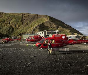 Three red helicopters on sand helipads in front of Wireless Hill