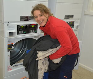 Woman in red sweater loading washing machine with sheets and smiling at camera