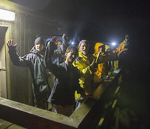 People standing on balcony of hut at night waving facing camera
