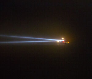 Ship in dark with two search lights shing to the left of frame