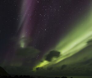 Green and purple coloured aurora in the sky above the beach at night