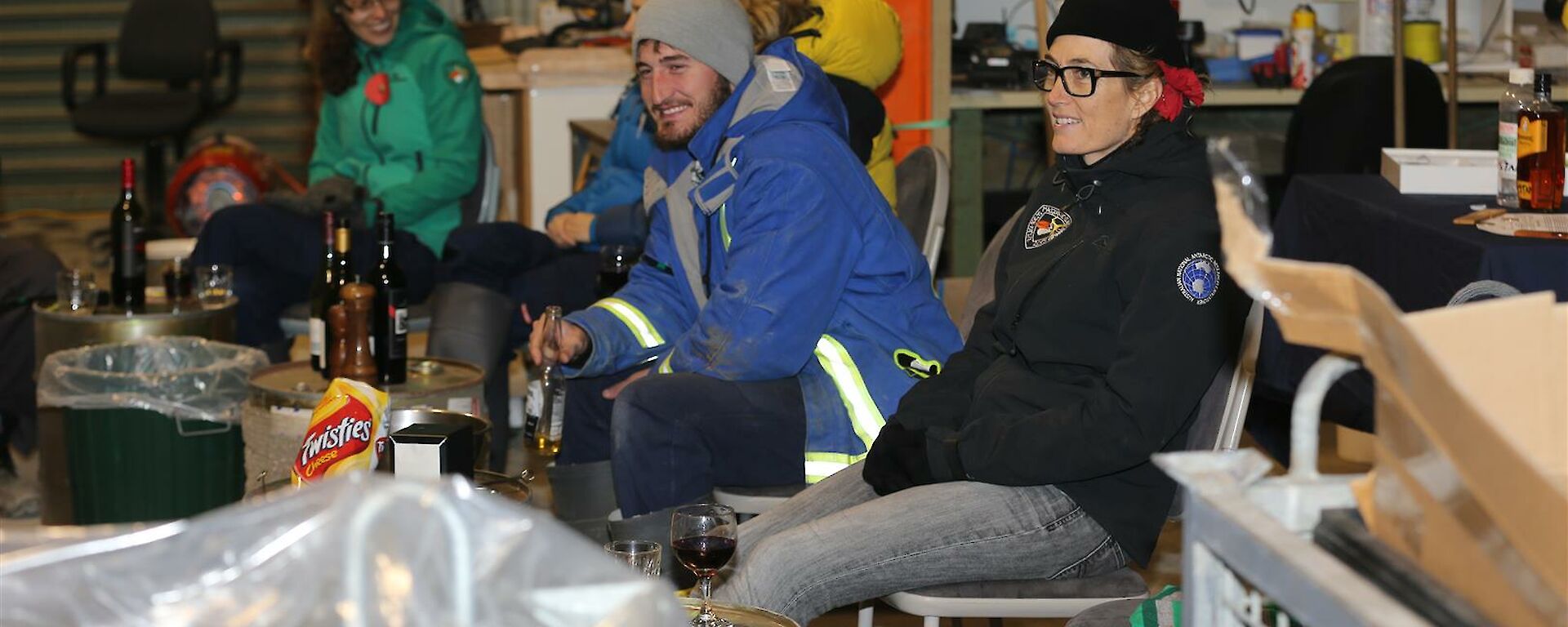 People sitting in shed with tools on wall in background talking and smiling