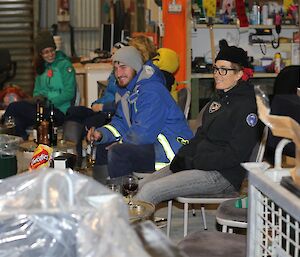 People sitting in shed with tools on wall in background talking and smiling