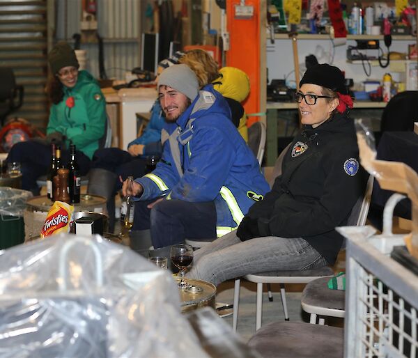 People sitting in shed with tools on wall in background talking and smiling