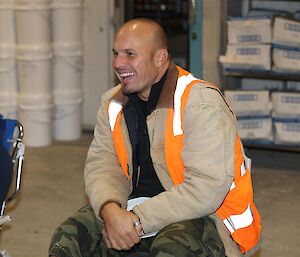 Man in brown jacket and orange vest seated and smiling