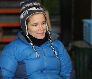 Woman in blue down jacket and beanie seated and smiling