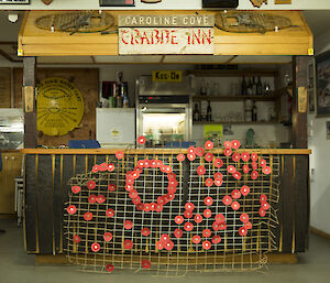 A metal mesh panel in front of a wooden bar with 100 red paper poppies attached