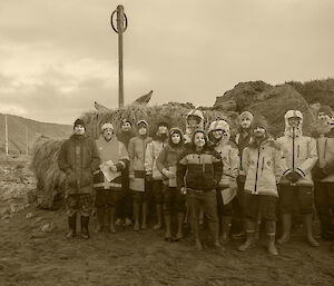 Group of expeditioners standing in front of a rock with Australian and New Zealand flags flying at half mast in the background