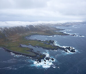 Aerial view of Macquarie Island’s northwest corner, with snow on the mountains and two rocky points jutting out into the sea