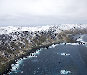 Aerial view of island with snow on mountain tops and a point jutting into the sea dividing two bays