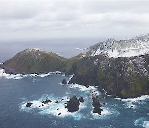 Aerial view of Macquarie Island with a hilly point jutting into the sea and several rocky stacks in the foreground