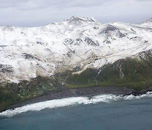 Aerial view of island with snow covered hills in background and a grey sandy bay in forground