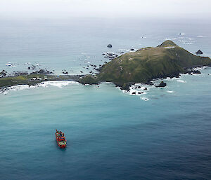 Aerial view of peninsula and narrow isthmus on which the station is located, with the red Aurora Australis supply ship anchored off the coast opposite the station