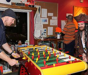 Two men in pirate costumes playing foosball