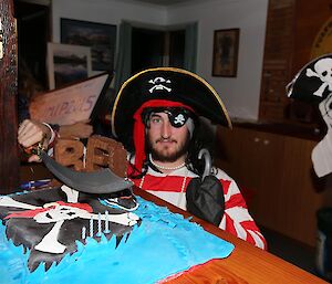 Man in red adn white striped shirt standing behind a birthday cake of a pirate flag