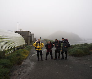 Four expeditioners standing on gravel road in fog with station buildings in the view