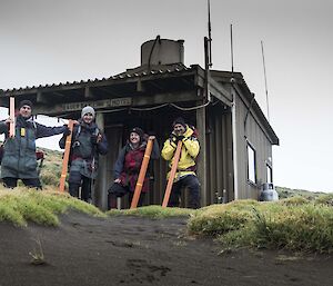 Four expeditioners standing in front of a hut holding orange poles
