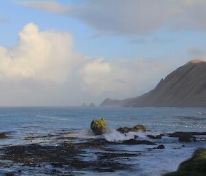 White fluffy clouds in a blue sky and mountainous coast in background