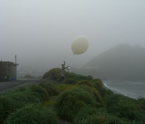 Expeditioner infog launching a weather balloon with hill in background