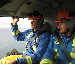 Two men in blue jackets and orange safety helmets sitting in helicopter with door open