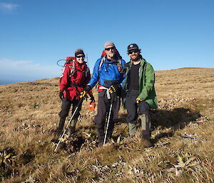 Three expeditioners standing in grass field and posing at camera