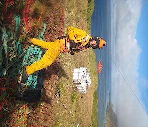 Man in yellow overalls smiling at camera with ocean and red ship in background