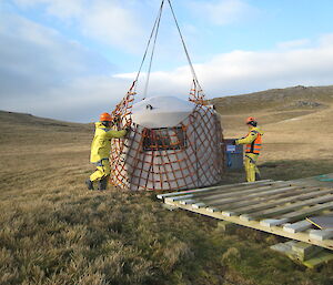 Two workers in yellow put water tank hut into red net