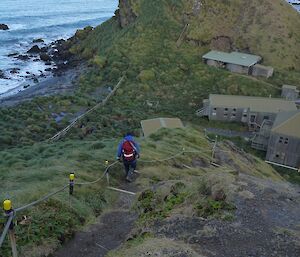 Man walking down track with station below and ocean in distance