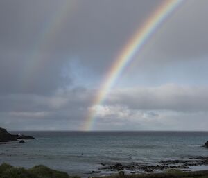 A rainbow out to sea with fence in forground