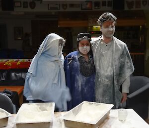 Three people dressed in sheets an covered in flour