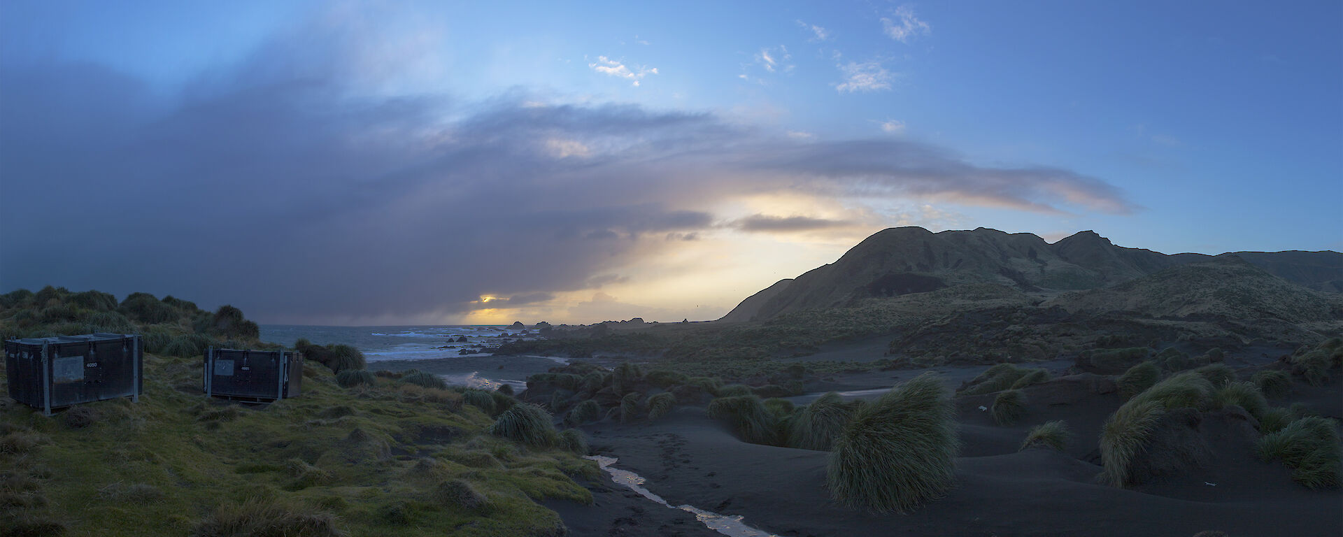 Sunset behind clouds with small creek in foreground and two cage pallet supply pods to the left