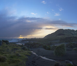 Sunset behind clouds with small creek in foreground and two cage pallet supply pods to the left