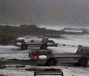 Two LARC land/sea vessels on a beach are taking on waves.