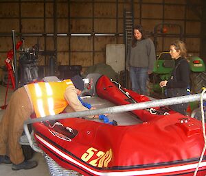 Three expeditoners surround an inflatable rubber boat in a big shed.