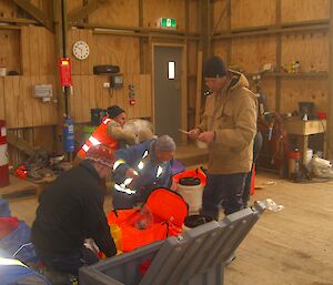 Four expeditioners in various positions check boating supplies inside a large shed.