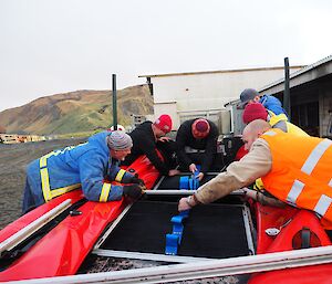 Six male expeditioners help put the floor of a rubber boat in.