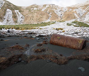 Rusting metal digester barrel with snowy hill behind and snow covered land slip path in centre of shot.